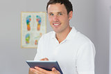 Handsome cheerful physiotherapist holding tablet