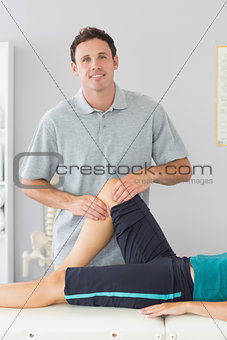 Smiling physiotherapist controlling knee of a patient