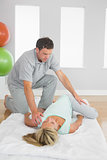 Physiotherapist examining patients hips on a mat on the floor