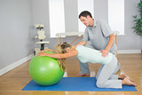 Physiotherapist controlling patient doing exercise with exercise ball