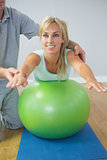 Physiotherapist holding patient doing exercise on exercise ball