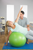 Smiling physiotherapist correcting patient doing exercise on exercise ball