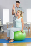 Physiotherapist correcting patient sitting on exercise ball
