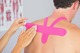 Physiotherapist putting on pink kinesio tape on male patients back