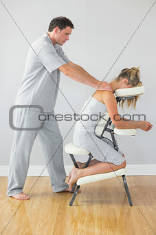 Masseur treating shoulders of client in massage chair