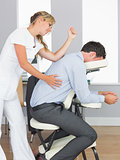 Masseuse treating clients back with elbow in massage chair