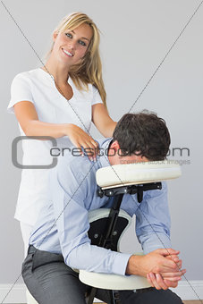 Smiling masseuse treating clients neck in massage chair
