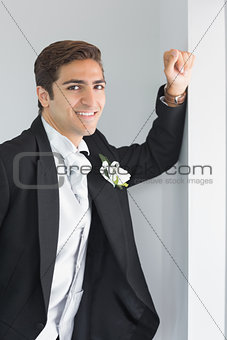 Cheerful young bridegroom leaning against wall