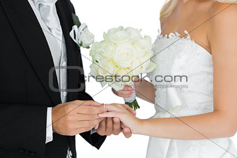 Young bridegroom putting on the wedding ring on his wifes finger