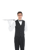 Cheerful young waiter showing an empty silver tray