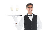 Smiling attractive waiter holding a tray with champagne glasses on it