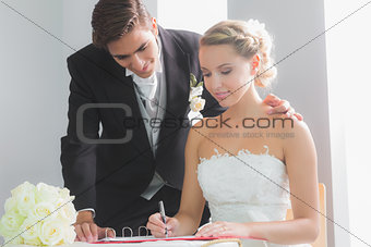 Young blonde bride sitting at table signing wedding register