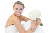 Happy blonde bride sitting on floor while holding a bouquet