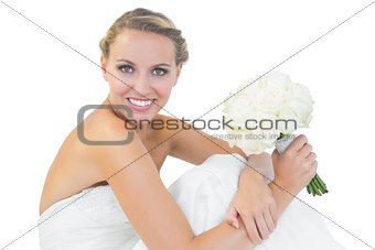 Happy blonde bride sitting on floor while holding a bouquet