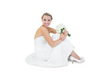 Pretty blonde bride sitting on floor holding a bouquet