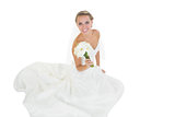 Cheerful young bride sitting on floor showing her bouquet