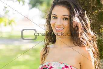 Stylish cheerful brunette leaning against tree
