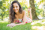 Stylish smiling brunette lying on a lawn looking at camera