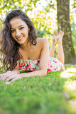 Stylish cheerful brunette lying on a lawn looking at camera