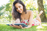 Stylish smiling brunette lying on a lawn using tablet