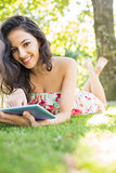 Stylish happy brunette lying on a lawn using tablet