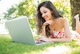 Stylish happy brunette lying on a lawn using laptop