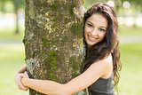 Casual cheerful brunette embracing a tree looking at camera