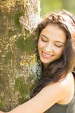 Casual smiling brunette embracing a tree with closed eyes