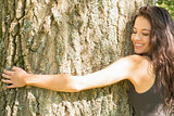 Casual happy brunette embracing a tree with closed eyes