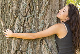 Casual content brunette embracing a tree with closed eyes