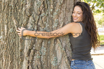 Casual attractive brunette embracing a tree with closed eyes