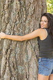 Casual attractive brunette embracing a tree looking at camera
