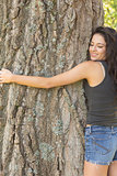 Casual beautiful brunette embracing a tree with closed eyes