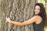 Casual beautiful brunette embracing a tree looking at camera