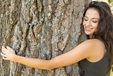 Casual gorgeous brunette embracing a tree with closed eyes