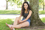 Casual happy brunette sitting leaning against tree