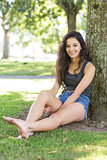 Casual smiling brunette sitting leaning against tree