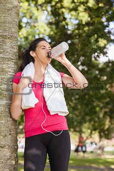 Sporty woman leaning against a tree and drinking