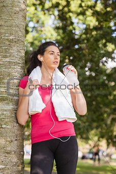 Beautiful sporty woman drinking water and leaning against a tree