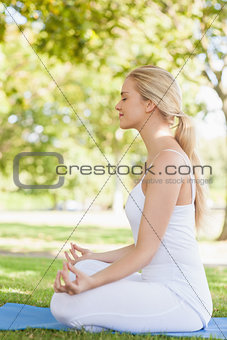 Side view of young woman meditating sitting on an exercise mat