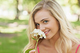 Beautiful blonde woman smelling a flower sitting in a park