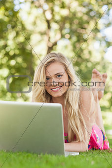 Cute woman using her notebook lying on a lawn