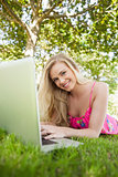 Portrait of beautiful young woman using her notebook lying on a lawn