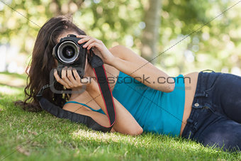 Front view of pretty brunette woman lying on a lawn taking a picture