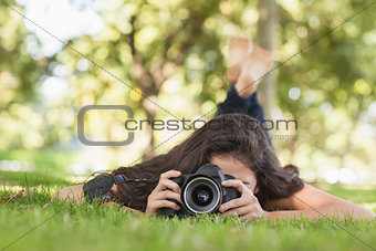 Young woman using her camera for taking a picture lying on a lawn