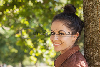 Beautiful young woman posing leaning against a tree