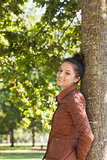 Side view of attractive brunette woman leaning against a tree