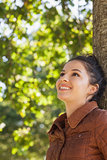 Side view of cheerful young woman leaning against a tree