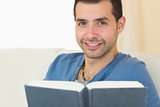 Casual smiling man sitting on couch holding a book