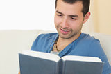 Casual smiling man sitting on couch reading a book